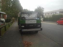 Ein grüner Lkw mit einem "Schrotthandel"-Schild parkt am Straßenrand.