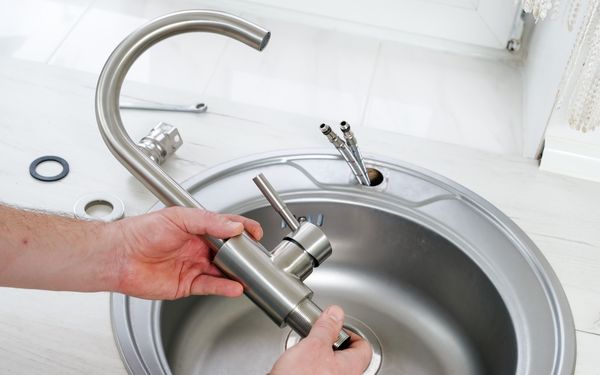 Ein Mann prüft, ob der Wasserhahn zum Anschluss des Waschbeckens passt.