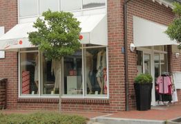 Modegeschäft mit Schaufensterpuppen, rotem Backstein und Markise.