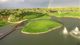 Golfplatz mit Inselgrün, umgeben von Wasser, Regenbogen im Hintergrund. Spieler sichtbar.