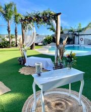 Jardín decorado para boda con pérgola de flores y mesa blanca junto a la piscina.
