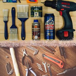 Werkzeuge und Malutensilien auf einem Tisch, darunter Pinsel, Bohrer, Dosen und Schraubenschlüssel.