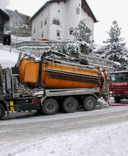 LKW und Feuerwehrfahrzeug im Schnee vor Häusern; Feuerwehrleute in Warnwesten sind zu sehen.
