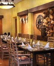 Interior de restaurante rústico con mesas y sillas de madera, decorado con ruedas de carreta.