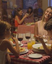 Familia cenando felizmente en restaurante con manteles de cuadros rojos y blancos.
