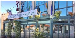 Fachada del Asador Villanueva con plantas y banderas junto a un edificio moderno.
