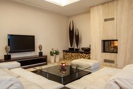 Modern living room with white sofas, glass table, flat-screen TV, and a fireplace.