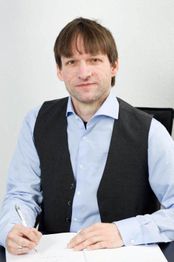 Ein Mann in Hemd und Weste sitzt am Tisch und schreibt mit einem Stift auf Papier.