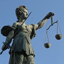 Statue of Justice holding a sword and scales against a clear blue sky.