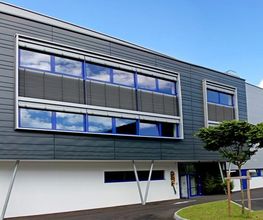 Edificio moderno con ampie finestre riflettenti e cielo blu sullo sfondo.