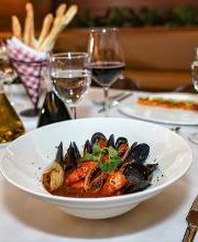 Plato de mariscos en salsa roja en mesa elegante con copas de vino y pan.