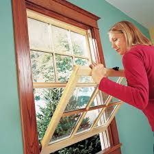 Person removing a window pane inside a room, with a tree visible outside.