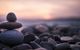 Stacked stones on a pebble beach with a soft, pink sunset in the background.