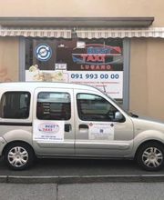 Silbernes Taxi parkt vor einem Schaufenster mit "Best Taxi Lugano" und einer Telefonnummer.