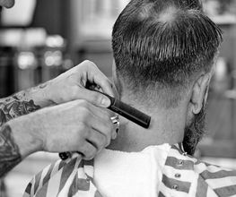 Barbiere taglia i capelli di un uomo con pettine e rasoio in un salone.
