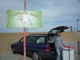 Frau steht neben Auto am Strand unter einem Schild mit der Aufschrift "Wattführerin Jessica".