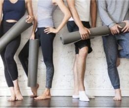 Personas con colchonetas de yoga, descalzas, apoyadas en una pared blanca.