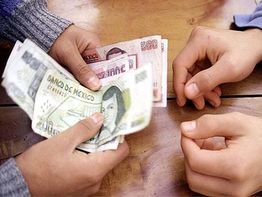 Manos intercambiando billetes de pesos mexicanos sobre una mesa de madera.
