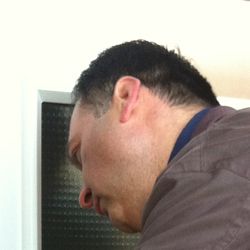 Mann in brauner Jacke beugt sich über eine Tür mit Glas.