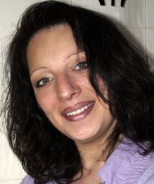 Eine Frau mit dunklem Haar und lila Hemd lächelt in die Kamera.