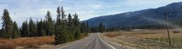 Open road in rural landscape with trees and mountains in the distance under a cloudy sky.