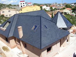 Casa de ladrillo con techo oscuro, ventanas inclinadas y fondo urbano.