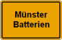 Ortsschild mit der Aufschrift „Münster Batterien“ vor gelbem Hintergrund.
