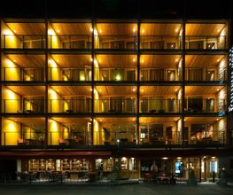 Beleuchtetes Hotelgebäude bei Nacht, mit offenen Balkonen auf mehreren Etagen.