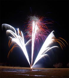 Feuerwerk am Nachthimmel mit bunten Lichtstreifen und leuchtenden Funken über einem Feld.