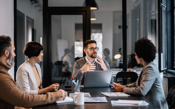 Vier Mitarbeitende besprechen gemeinsam Arbeitsthemen bei einem Meeting mit Laptop und Unterlagen.