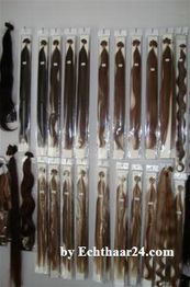 Verschiedene Haarverlängerungen in unterschiedlichen Braun- und Blondtönen hängen an der Wand.