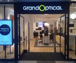 Winkelpui van een opticien met het bord "Grand Optical" en een welkomstdisplay aan de zijkant.
