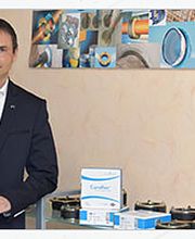 Ein Mann steht neben einem Curaflex-Werbeplakat und Produkten auf einem Tisch.