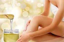 Person beim Eincremen ihrer Beine mit Öl, goldener Hintergrund, entspannte Atmosphäre.