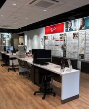 Interieur van een brillenwinkel met houten vloer, tafels en bril displays aan de muren.