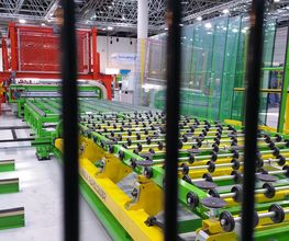 Industrielle Fertigungsanlage mit grünen Maschinen und Förderbändern hinter schwarzen Gittern.