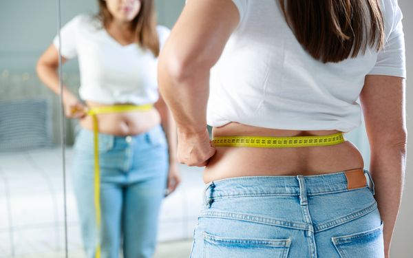 Frau misst ihre Taille mit einem Maßband während ihrer Abnehmreise.