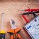 Tools for electrical work on a wooden surface, including a screwdriver and multimeter.