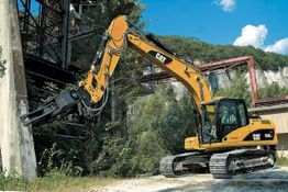 Ein Bagger mit hydraulischem Greifer bearbeitet eine Betonwand in industrieller Umgebung.