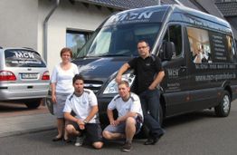 Vier Personen posieren vor einem Firmenwagen auf der Straße.