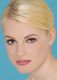 Eine Frau mit blonden Haaren und Make-up schaut in die Kamera vor blauem Hintergrund.