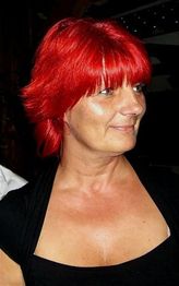 Eine Frau mit leuchtend roten Haaren blickt nach rechts und trägt ein schwarzes Oberteil.