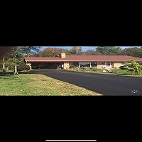 Single-story house with a red roof, large driveway, and a green lawn.