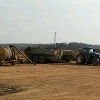 Tractor with trailers on a dirt field under a cloudy sky.