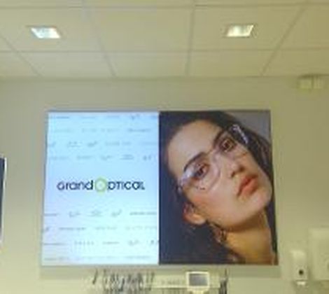 Poster aan de muur van een opticien met merklogo en een vrouw die een bril draagt.