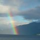 Arcobaleno sul mare con montagne e cielo nuvoloso.