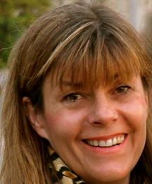 Eine Frau mit schulterlangem Haar lächelt in die Kamera. Sie trägt einen gemusterten Schal.