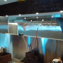 Large commercial kitchen with stainless steel appliances and bright overhead lights.