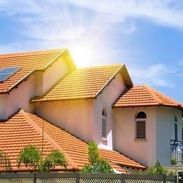 House with red roof under sunny sky, lush greenery in foreground.