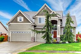 Modern suburban house with a spacious driveway, green lawn, and blue sky background.